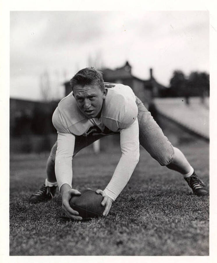 Freshman football player for the University of Idaho Jim Swarbrick crouching over a football on the field.
