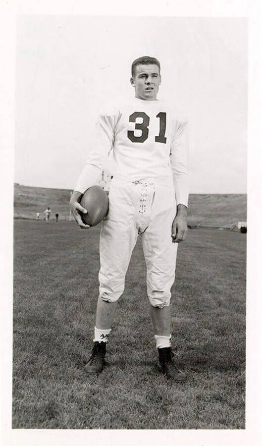 Dick Pickett, a freshman on the University of Idaho football team, standing on the field with a ball.