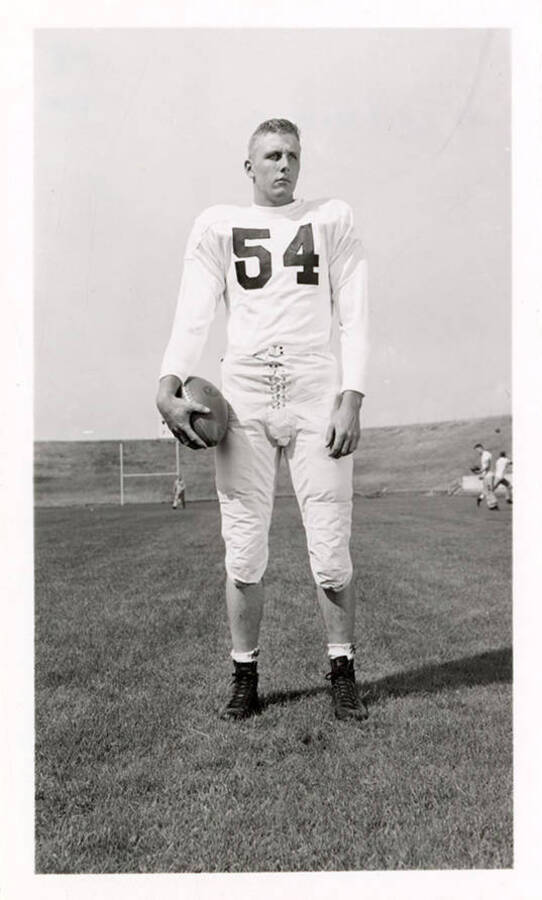 Freshman University of Idaho football player, Don Wisdom (#54), standing and holding a football.