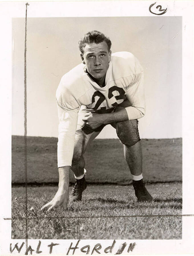 Football player, Walt Hardin (#23), end for the University of Idaho, crouching with a hand on the football field.