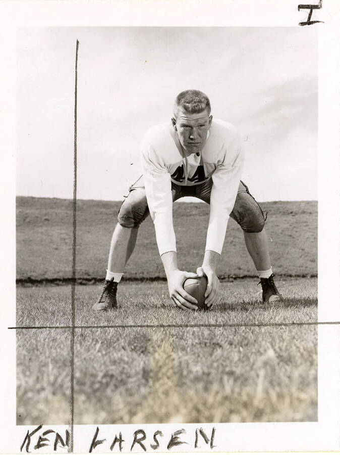 Ken Larsen (#44), center for the University of Idaho football team, crouching with his hands on a football.