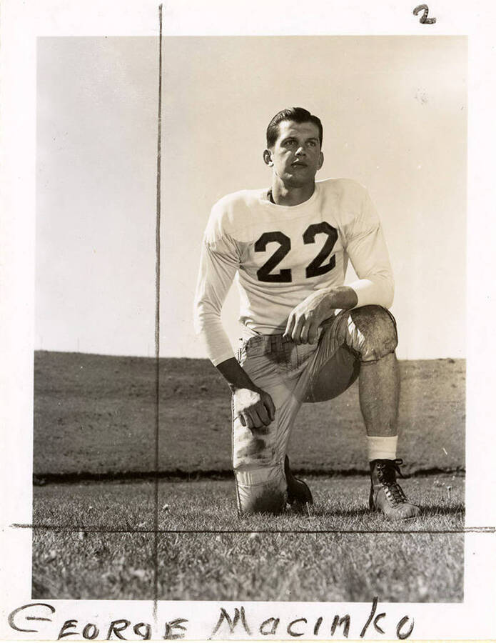 George Macinko (#22), end for the University of Idaho football team, kneeling on the football field.