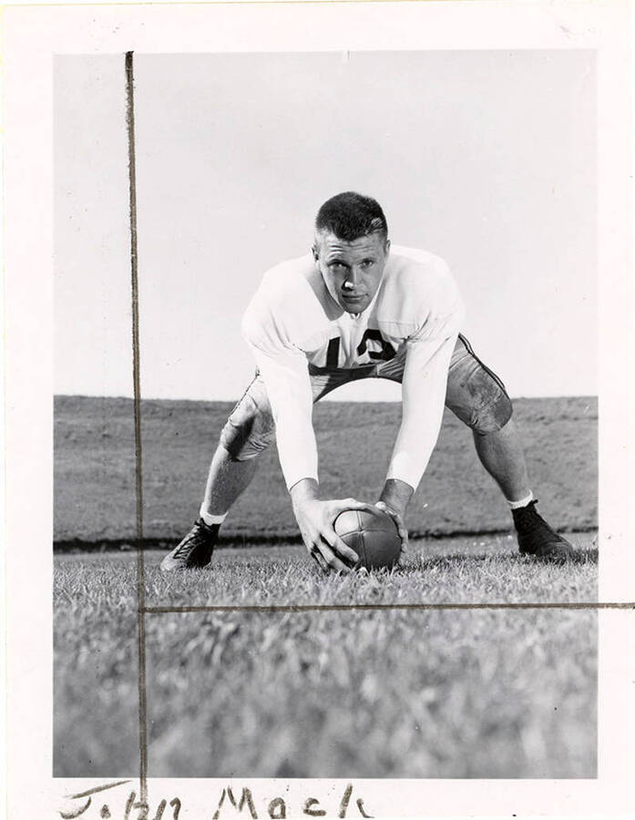 John Mack, center for the University of Idaho football team, crouching with his hands on a football placed on the field.