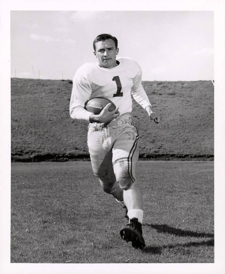 Dave Murphy (#1), right halfback for the University of Idaho football team, running with a football on the field.