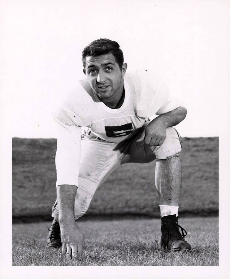 Left halfback for the University of Idaho football team, Jim Petruzzi (#5), kneeling with one hand on ground.