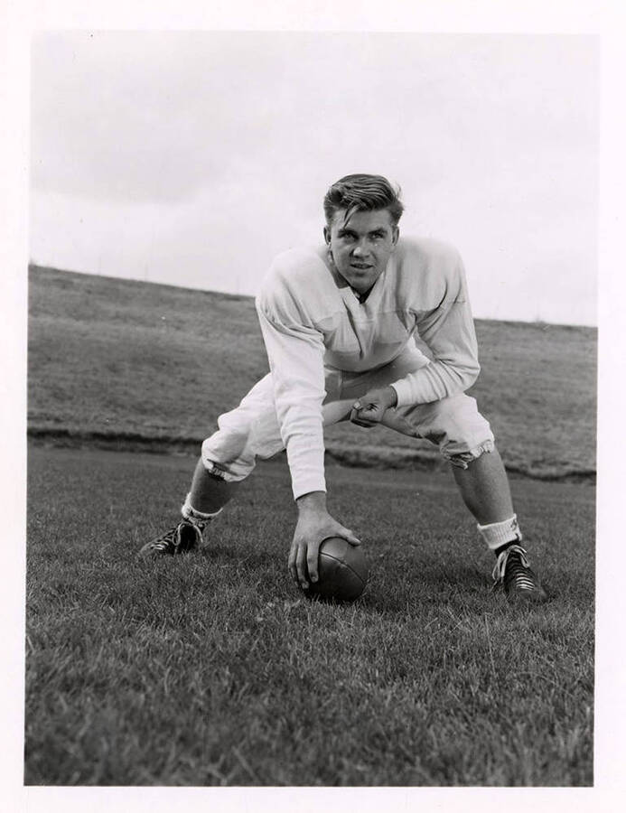 Bill Stellmon, a guard for the University of Idaho, crouching on the field with a football.