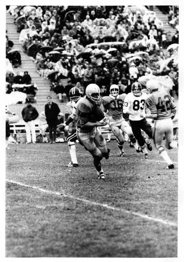 An opposing player runs with the ball from the University of Idaho football players during a game as an audience watches from the bleachers.