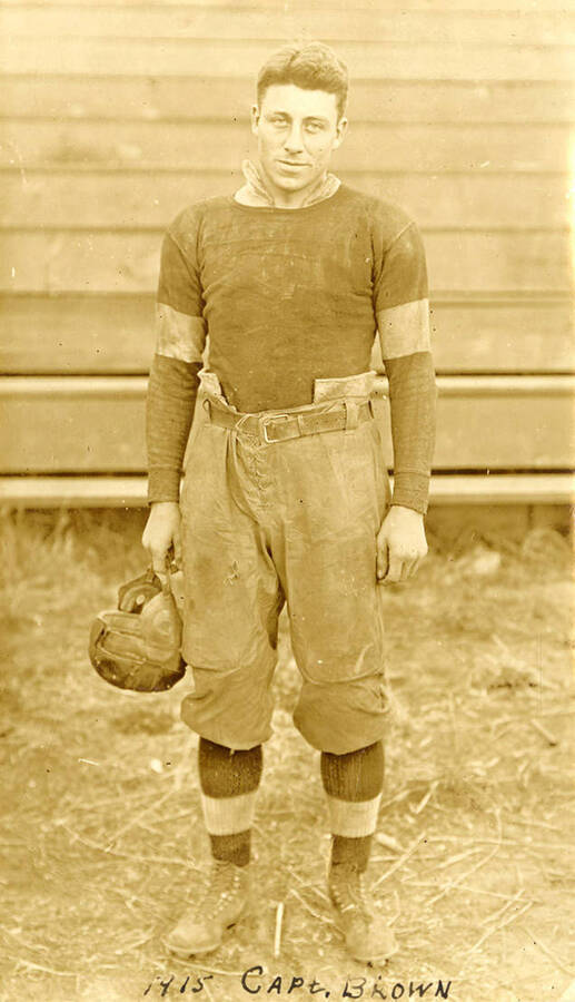 University of Idaho football team's Captain Brown standing in uniform and holding his helmet for a portrait photograph.