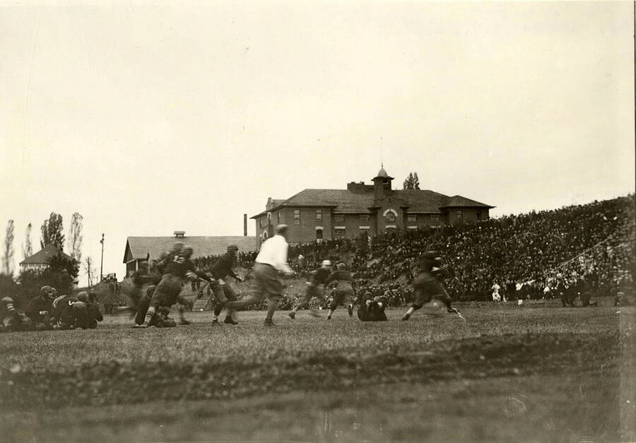 Football players run and tackle as the referee monitors during a football game at the University of Idaho with a full audience.