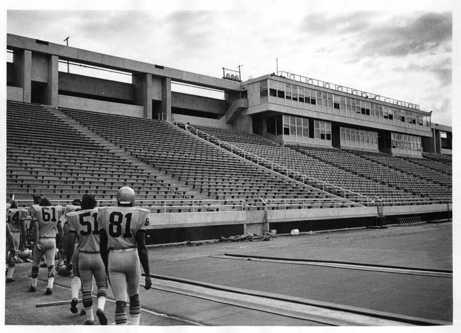 University of Idaho football players in full uniform walk onto the football field surrounded by empty bleachers.