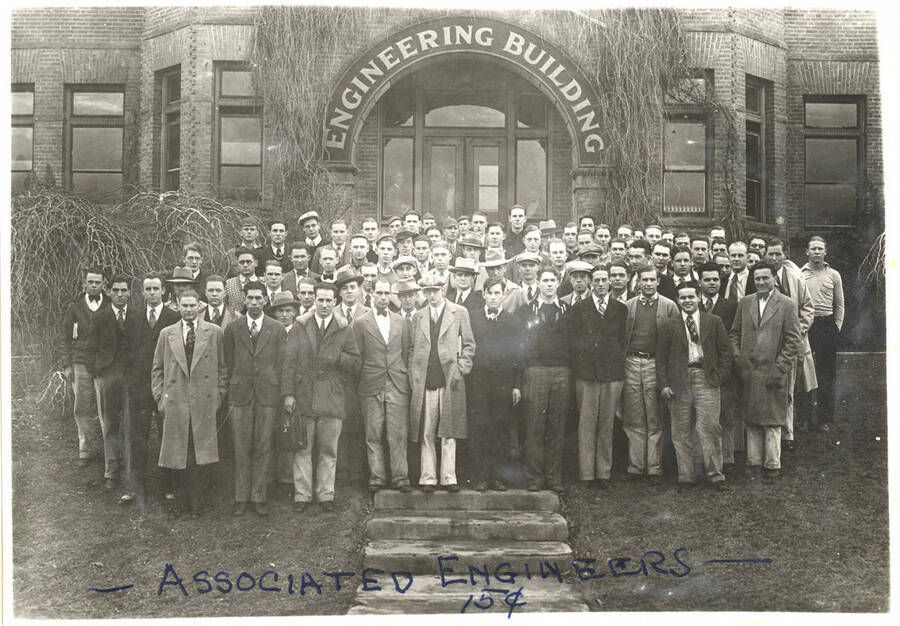 Members of the Associated Engineers pose together on the steps in front of the Engineering Building at the University of Idaho. Caption reads '~Associated Engineers~ 15 cents'.