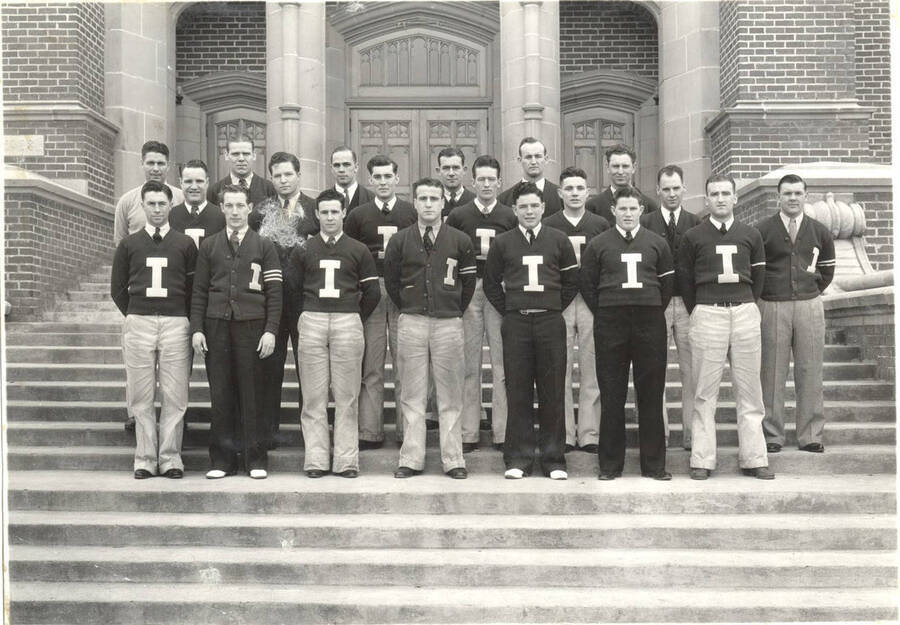I Club members standing for a group photo in front of the Memorial Gym. Back: L. Calland, J. Barbee, P. Berg, R. Villers, R. Nutting, L. Albee; middle: R. Sundberg, J. Wheeler, M. Fisher, G. Naslund, W. Geraghty, L. Anderson, C. Wilson; front: H. Schodde, C. Geraghty, C. Devlin, R. Honoswetz, L. Green, J. Cooper, H Swann