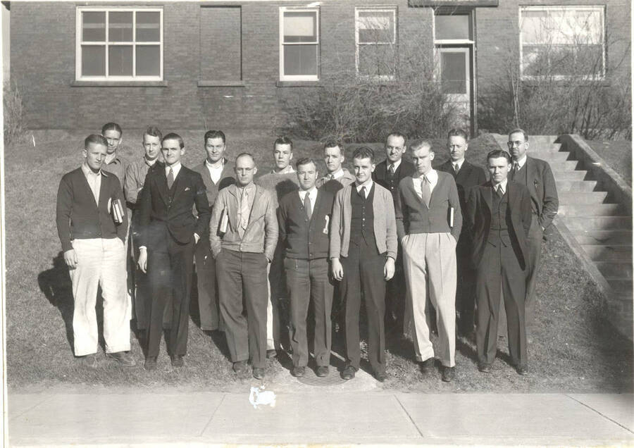 Sigma Gamma Epsilon members stand in front of an unidentified building for a group photo. Sigma Gamma Epsilon is a national professional mining fraternity. Individuals identified as listed. Front: E. Leatham, J. Wells, William Lundstrum, C. March, D. Larsen, A. Nelson, V. Hammerand; back: F. Danielson, E. Hayes, R. Humphreys, R. Quinsrom, E. Kroll, A. W. Fahrenwald, A. L. Anderson, W. Staley