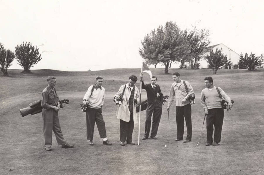 Golf team members stand on the golf course with their gear. Individuals identified from right to left: Bill Holzer, Charles Taylor, Sunday Provenzano, Bob Smith, Stan Jones, Rudy Franklin.
