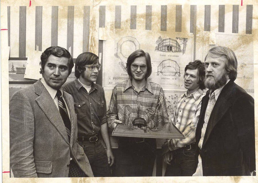Five men surround a winning scale-model of a building comprised of wood, likely of locally harvested species.