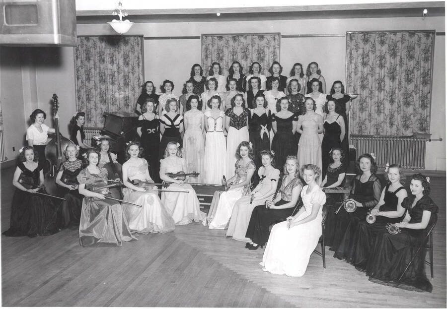 All-women orchestra and chorus pose for a photo with instruments.