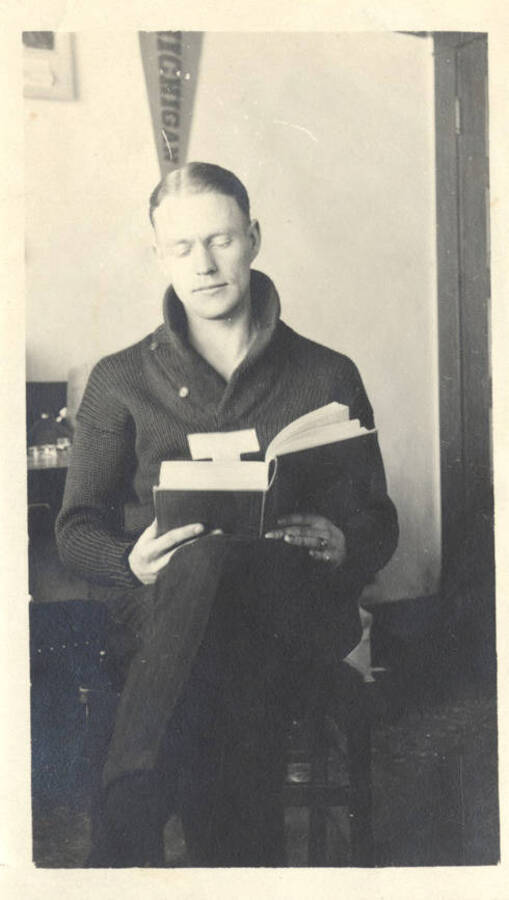 An unidentified student reads a book in his dorm room. The inscription on the back of the photograph reads 'A student - of nothing!'