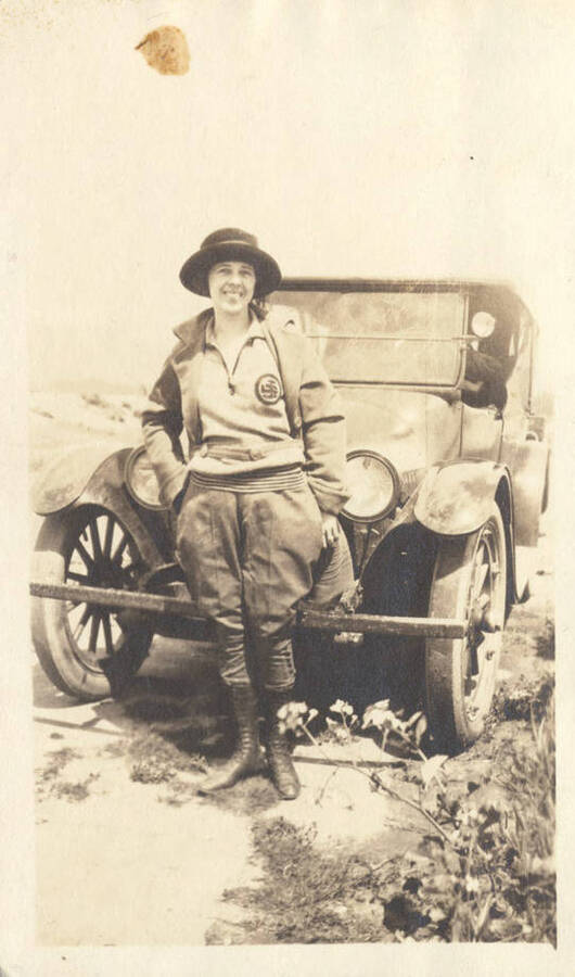 An unidentified woman stands in front of an automobile.