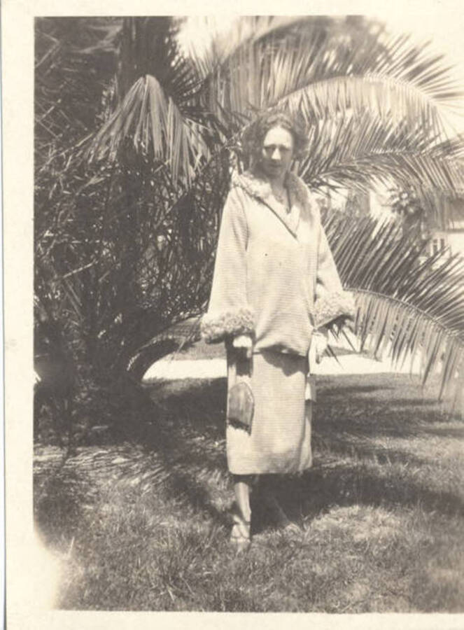 An unidentified woman stands next to a palm tree in a fashion coat.