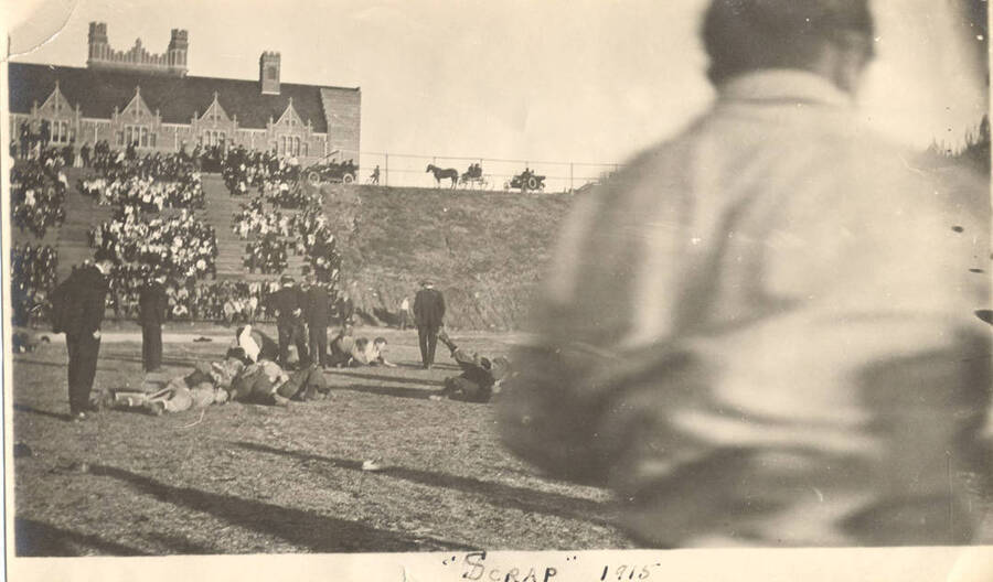Students wrestle on the football field while bystanders referee. Caption reads ''Scrap' 1915'