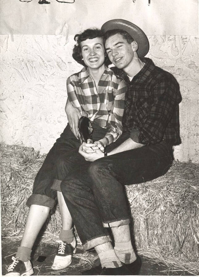 An unidentified greek couple dressed in Western themed clothing poses for a photo on staged hay-bales.