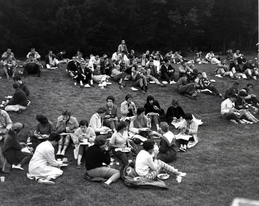 Students sitting on the grass, eating their food from the all campus barbecue at the old arboretum.