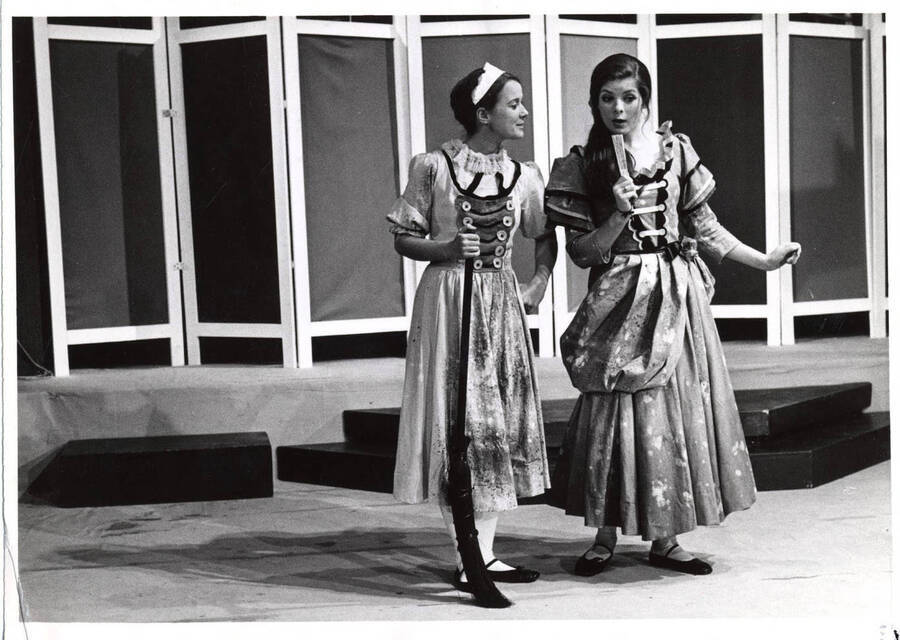 Two women perform on stage in costumes.