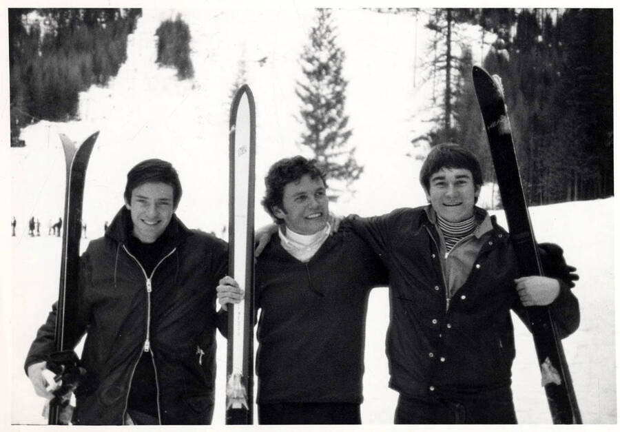 Three skiers pose for a group photo in the snow with their ski equipment in hand.
