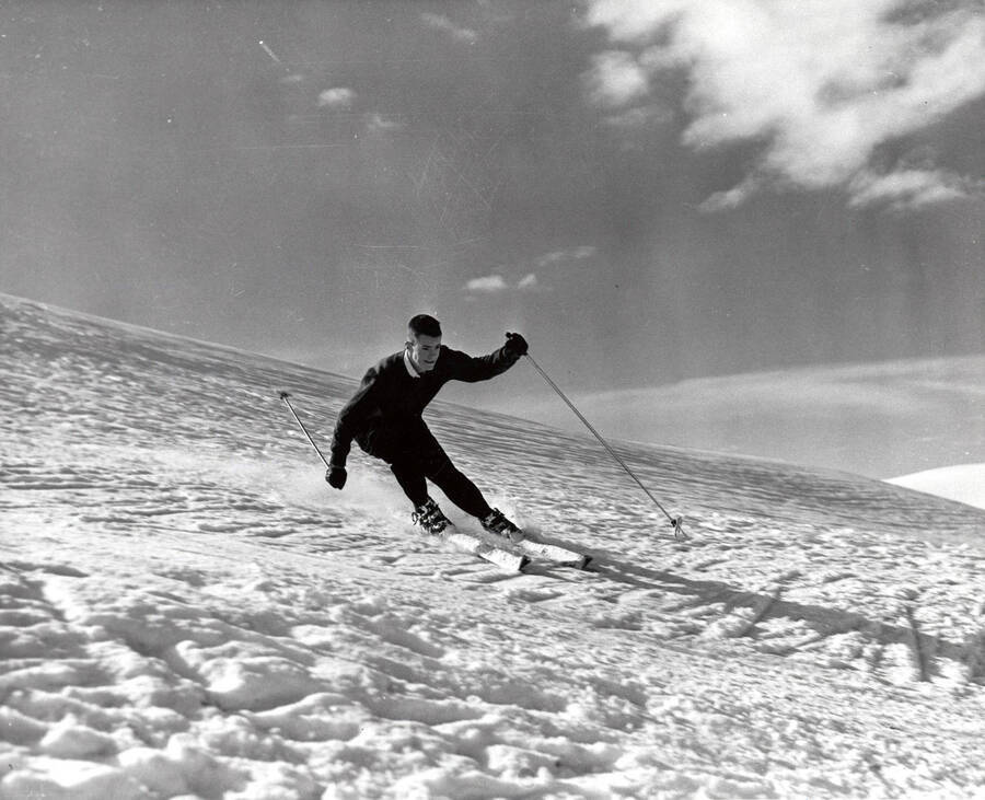 An unidentified man skis down a snow covered hill, mid slalom.