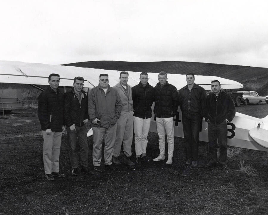 Members of the Vandal Flying Club stand near the tail of a Piper PA-20 Pacer aircraft posing for a photo.