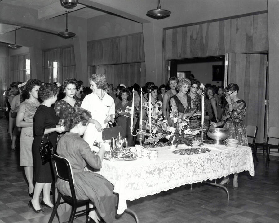 Women wait in line for beverages during the Freshman women's tea. One woman is seated with her back to the camera serving tea to women in line.