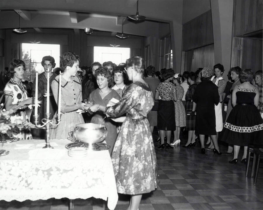 Women serve themselves from a punch bowl at the Freshman women's tea while others find seats in the background.