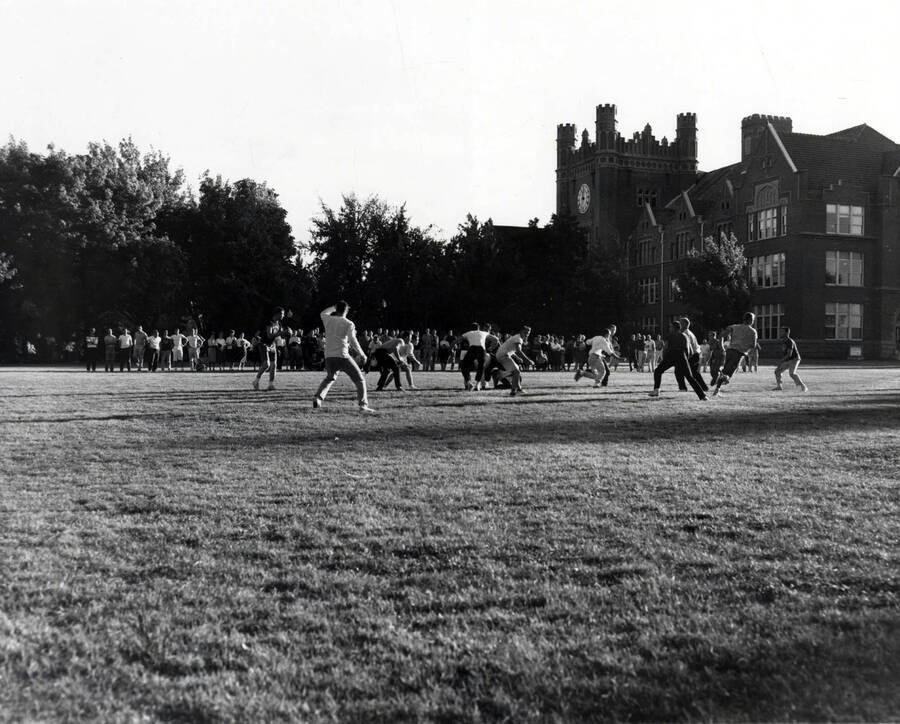 Intramural touch football teams play on the Administration lawn while an audience watches.