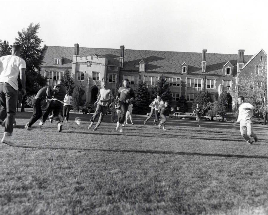 Men play touch football on the Administration lawn with the Life Sciences (South) building visible in the background.