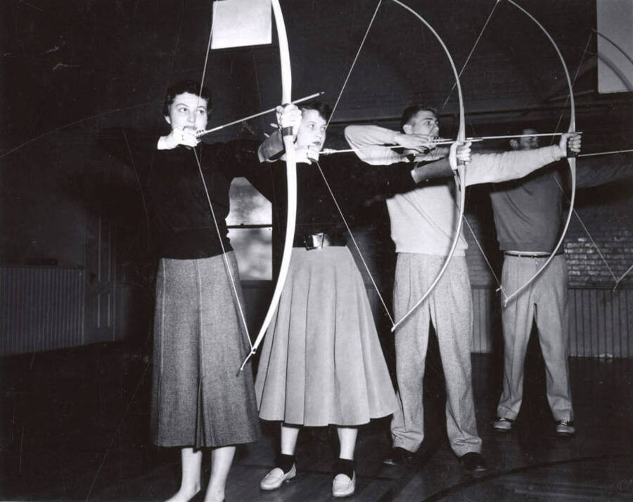 Two men and two women draw their bows and aim during archery class.