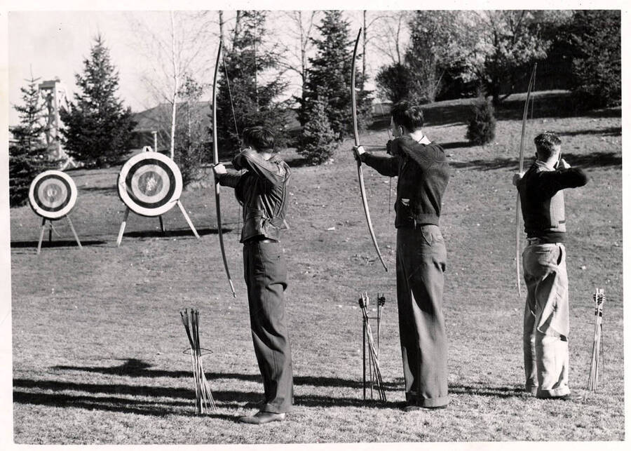 Three men aim at targets with drawn bows during archery class.