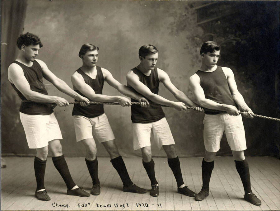 The champion 600' tug-of-war team poses for a photo using a rope to mimic a tug-of-war. Individuals identified from left to right: Edmund Roy Greenslet, George Christian Leth, Earl Arthur Beck, Lewis Hull Bowman.