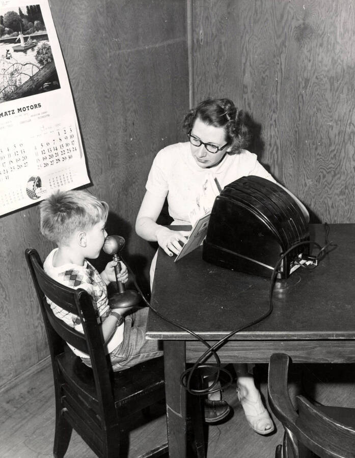 Lois Stone, University of Idaho graduate student, works with a child in the Summer Child Guidance Clinic. The child is speaking into a microphone while Lois Stone watches.