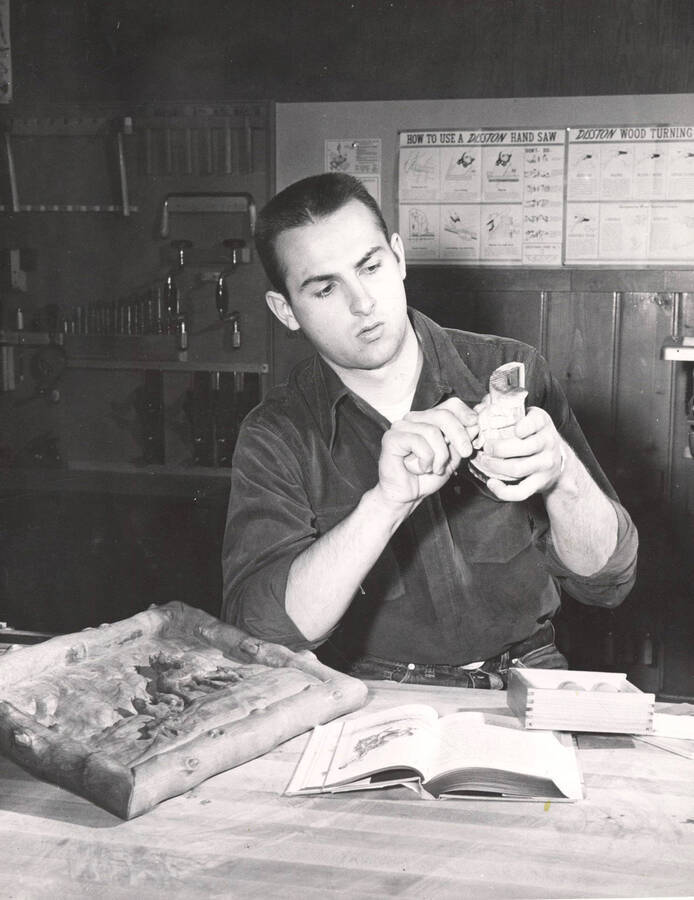 Larry Elsner, an Industrial Arts Education student, works with a wooden object with a book open in front of him.