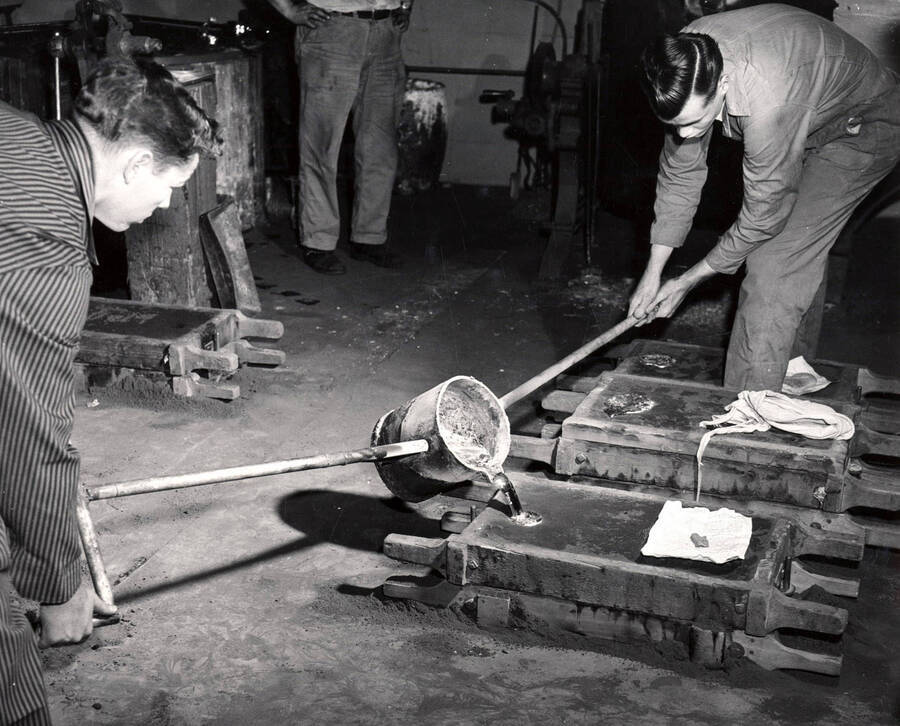 Gene Baxter and Arvin Vawter pour molten metal into a sand mold form.