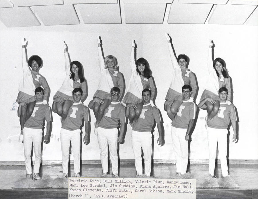 A group photo of the Rally Squad with the men holding the women on their shoulders. Individuals identified as listed: Patricia Kido, Bill Millick, Valerie Plum, Randy Luce, Mary Lee Strobel, Jim Cuddihy, Diana Aguirre, Jim Hall, Karen Clements, Cliff Bates, Carol Gibson, Mark Shelley.