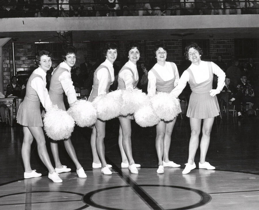 The Pom-Pom Girls pose with their poms in a group huddle in the Memorial Gymnasium during a basketball game.
