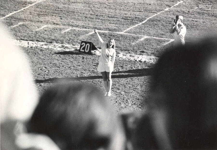 A photograph taken from the crowd shows a Pom-Pom Girl cheering on the sidelines of MacLean Field.