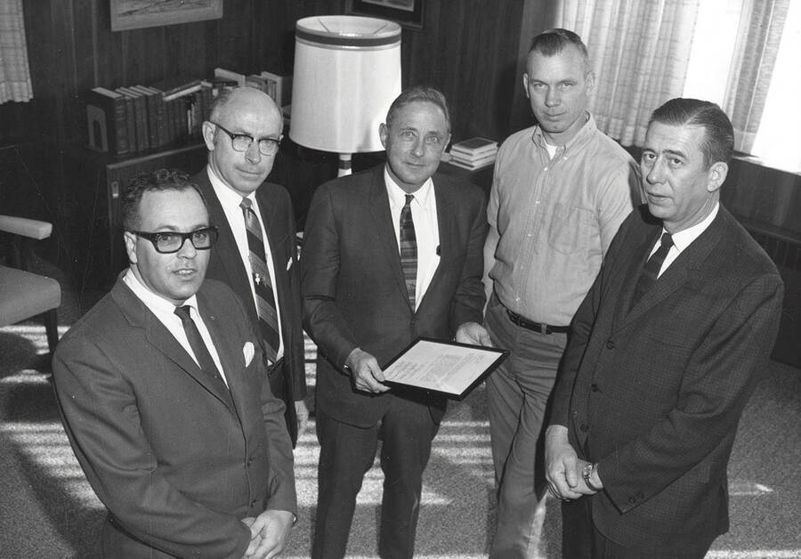 President Ernest Hartung receives a formal letter of appreciation for his accomplishments and policies. Individuals identified as listed from left to right: Dick Beck, William P. Barnes, Dr. Hartung, Martin Rathbun, E.V. Samuelson. Copy of letter on back of mount