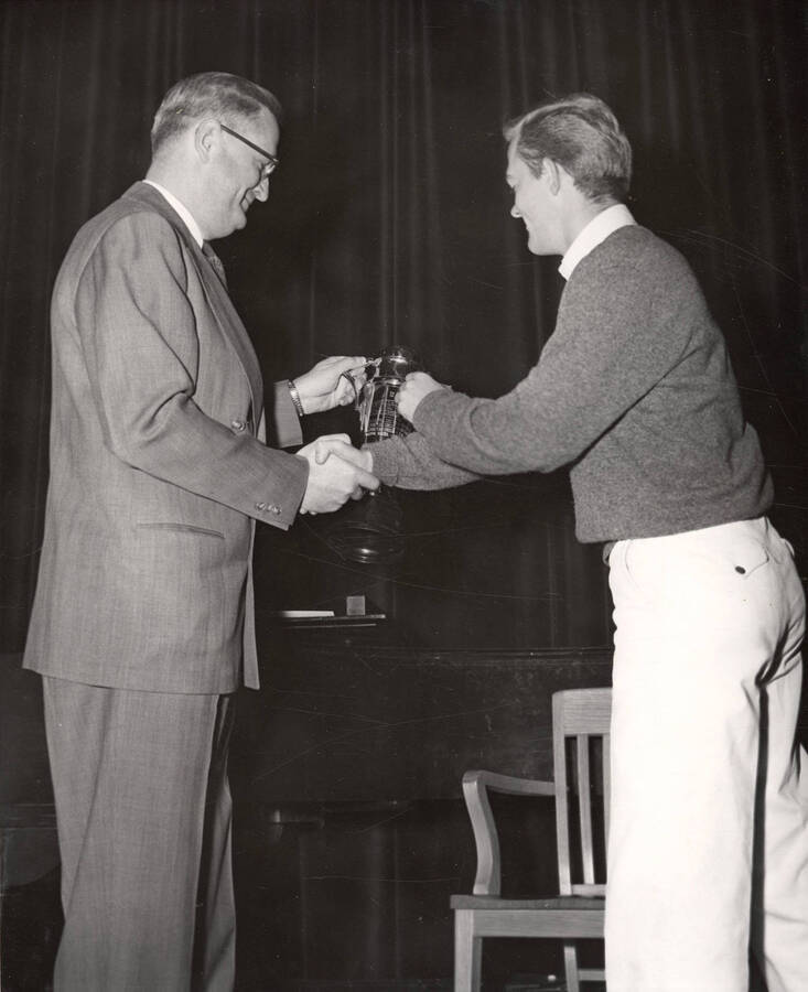 University of Idaho student Donald Clark, president of Kappa Sigma fraternity, accepts the Interfraternity Council trophy from University of Idaho President Jesse E. Buchanan.