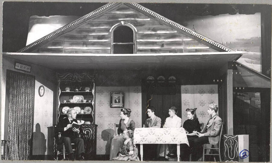 From l-r: Richard Pennell as Mr. Hyde, Marjorie Dean as Mama, Pat Blessinger as Dagnar, Mac Parkins as Nels, Lillian Bowler as Trina, Polly Garst as Christing, and Richard Peterson as Papa. Mr. Hyde reads a book to the rest of the party in a scene of Idaho drama's production of 'I Remember Mama.'
