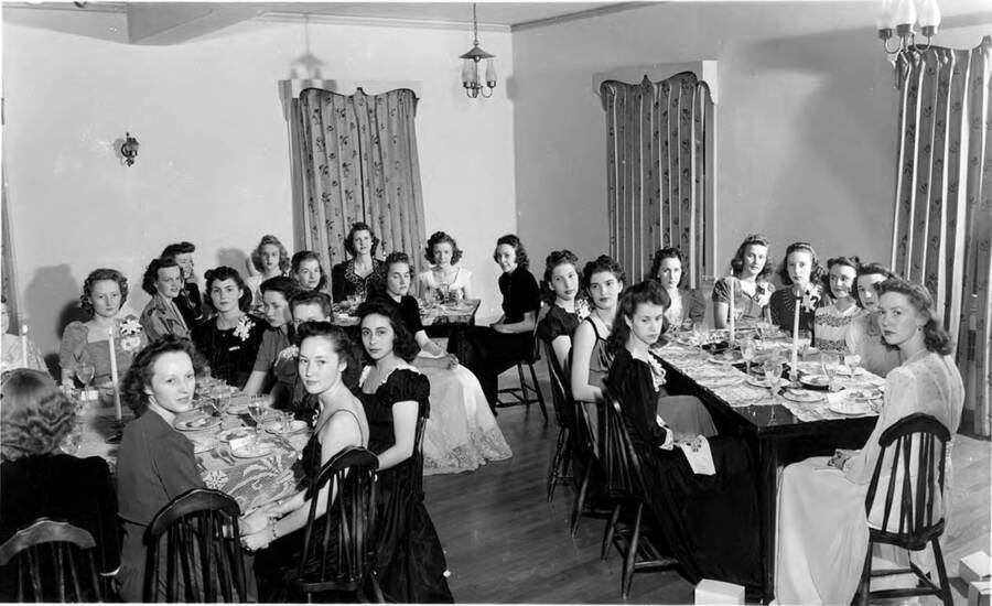 Women of Delta Delta Delta sit down to eat at a formal dinner in the Delta Delta Delta house.