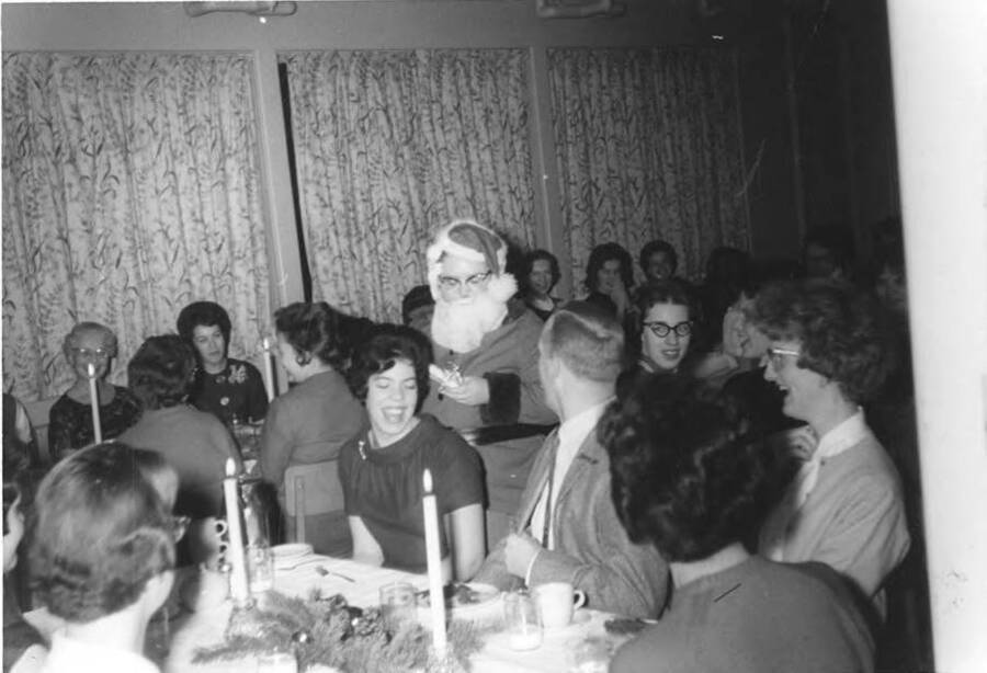 A group of people sit at tables during a Christmas party at Ethel Steel House. One person walks around the room dressed as Santa Claus.
