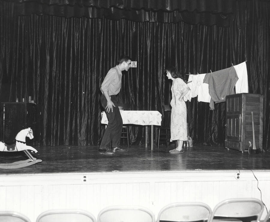 Two cast members perform together on stage during a drama production of 'Hello from Bertha'. Cast includes Sue Arms, Kyla Thomas, Chris Reynolds, and Phyllis Harris.