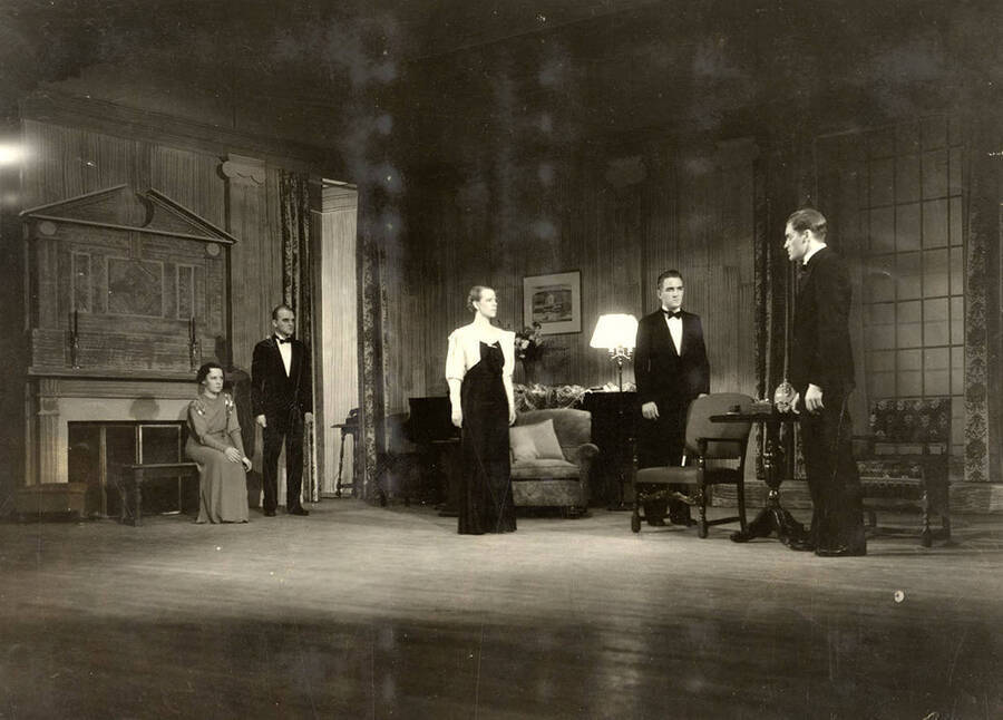 During the drama production of 'Dangerous Corner,' men and women stand on the stage. Cast: Robert Herrick as Gordon Whitehouse, Dorothy Pierce as Freda Chatfield, Eldred Stephenson as Robert Chatfield, Alline King as Olwen Peel, Paul Selby as Charles Stanton, Nina Varian as Betty Whitehouse, Ethlyn O'Neal as Maud Mockridge